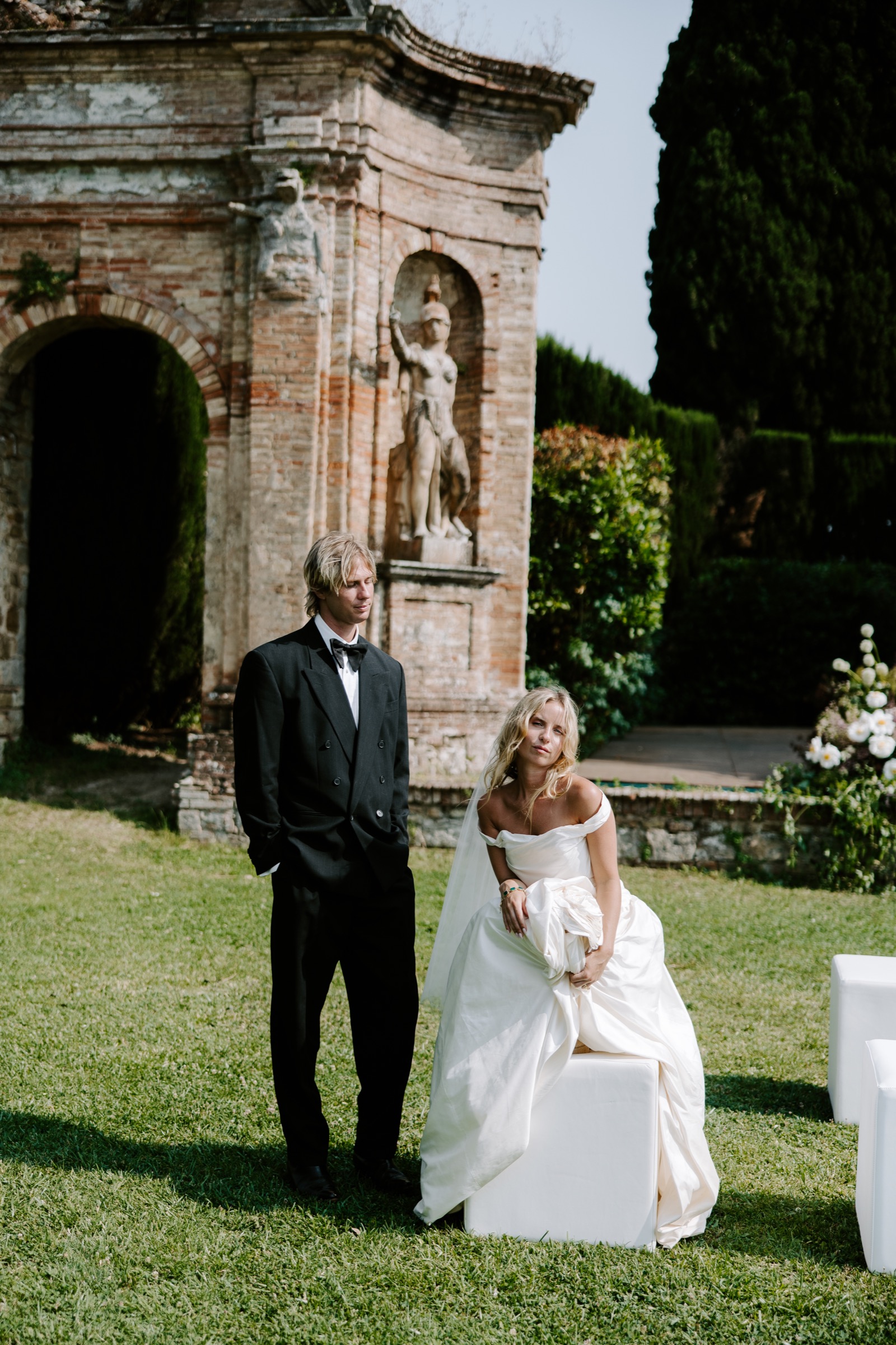 Bride and groom posing beside historic stone architecture in an Italian garden