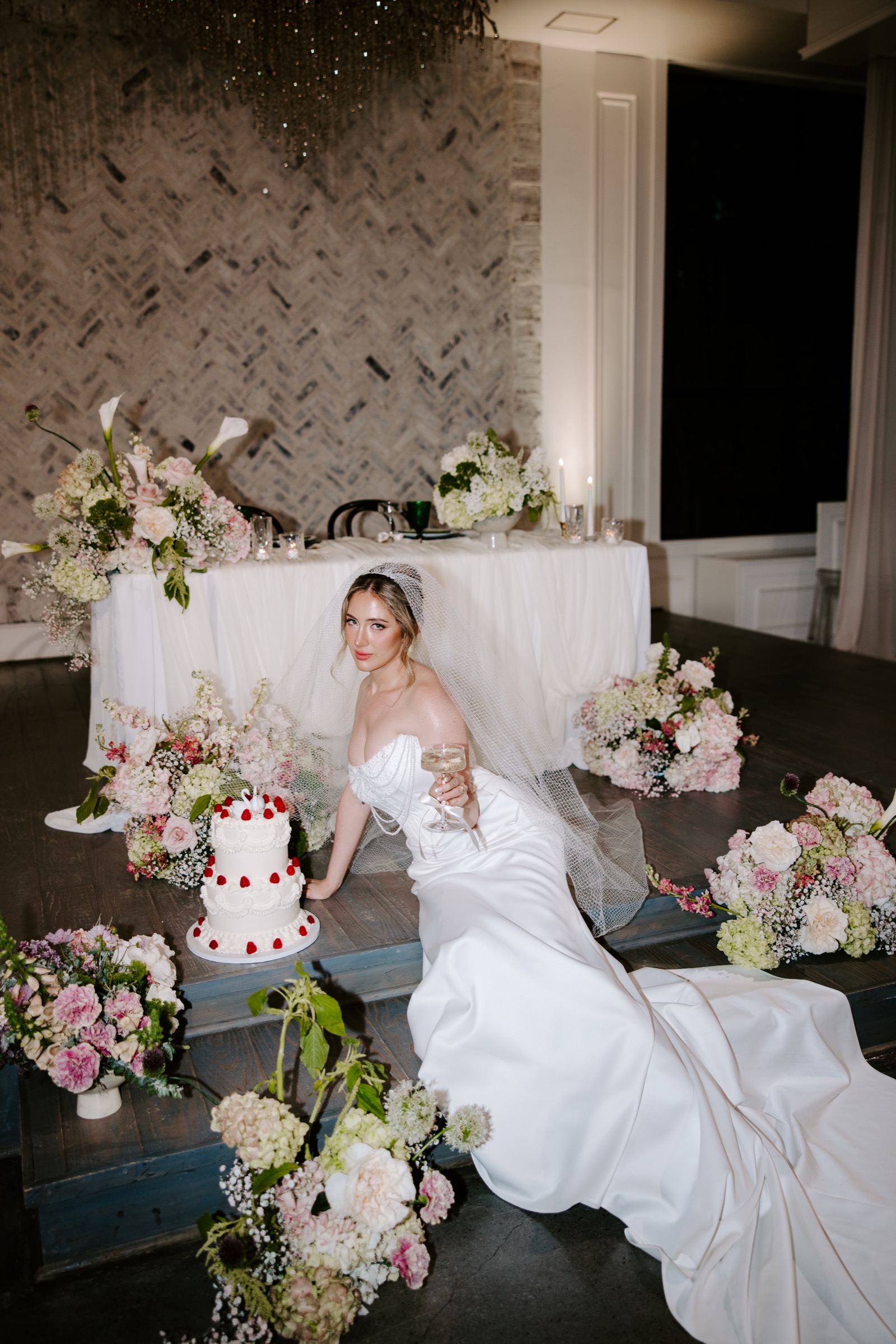 Bride with a champagne glass beside her wedding cake and flowers