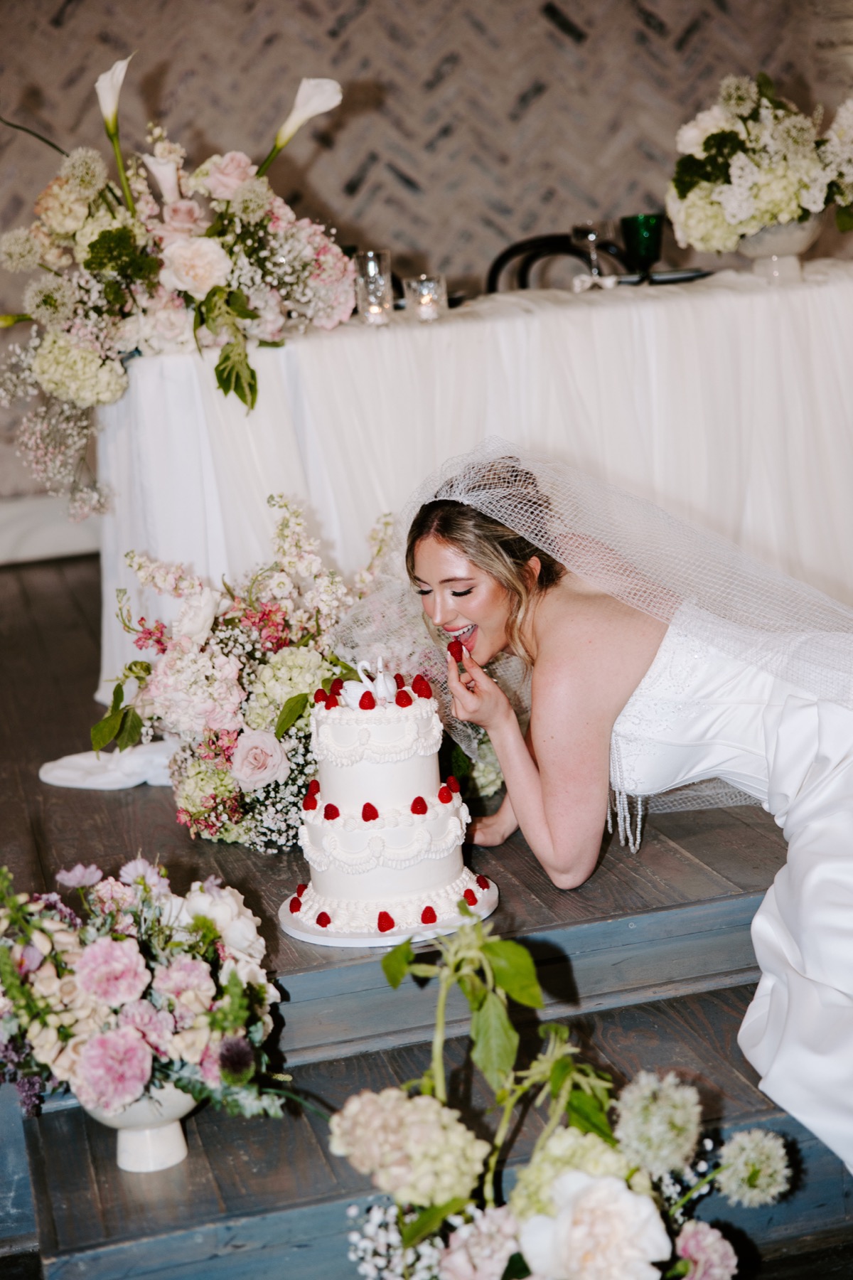 Bride enjoying a strawberry beside her flower-covered wedding cake