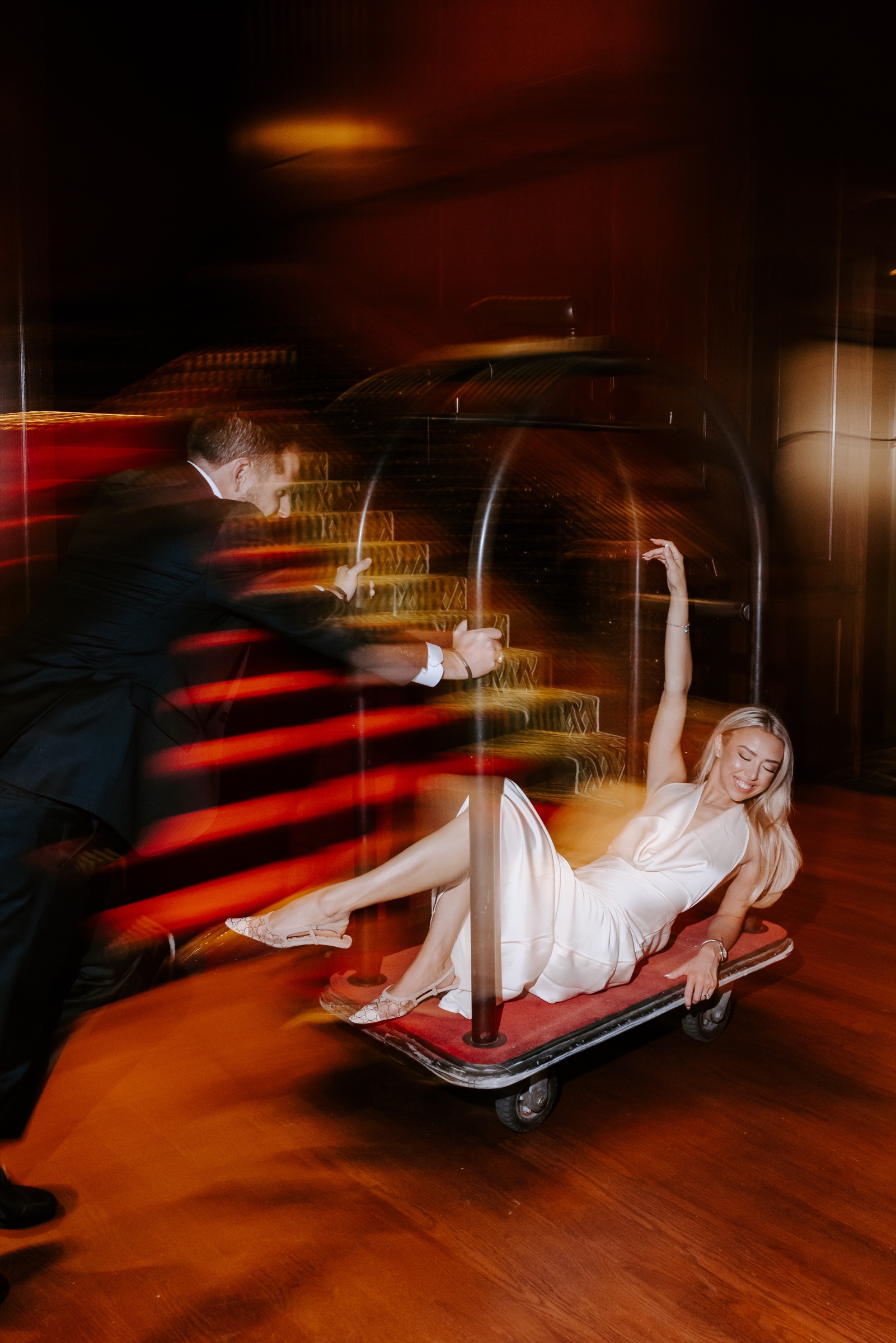 Bride celebrating on a hotel luggage trolley with her groom