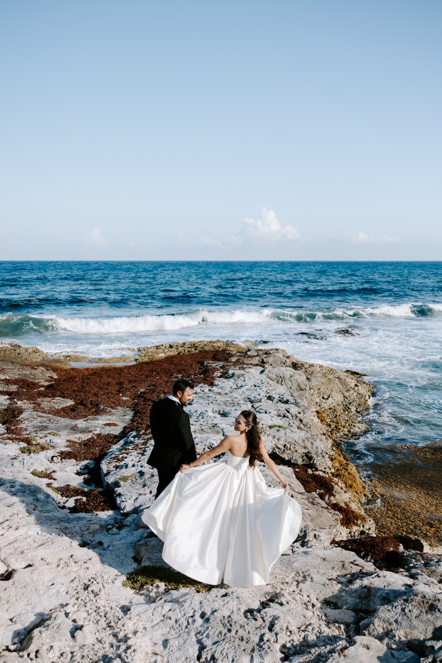 Newlyweds holding hands on a rocky coastline beside the ocean