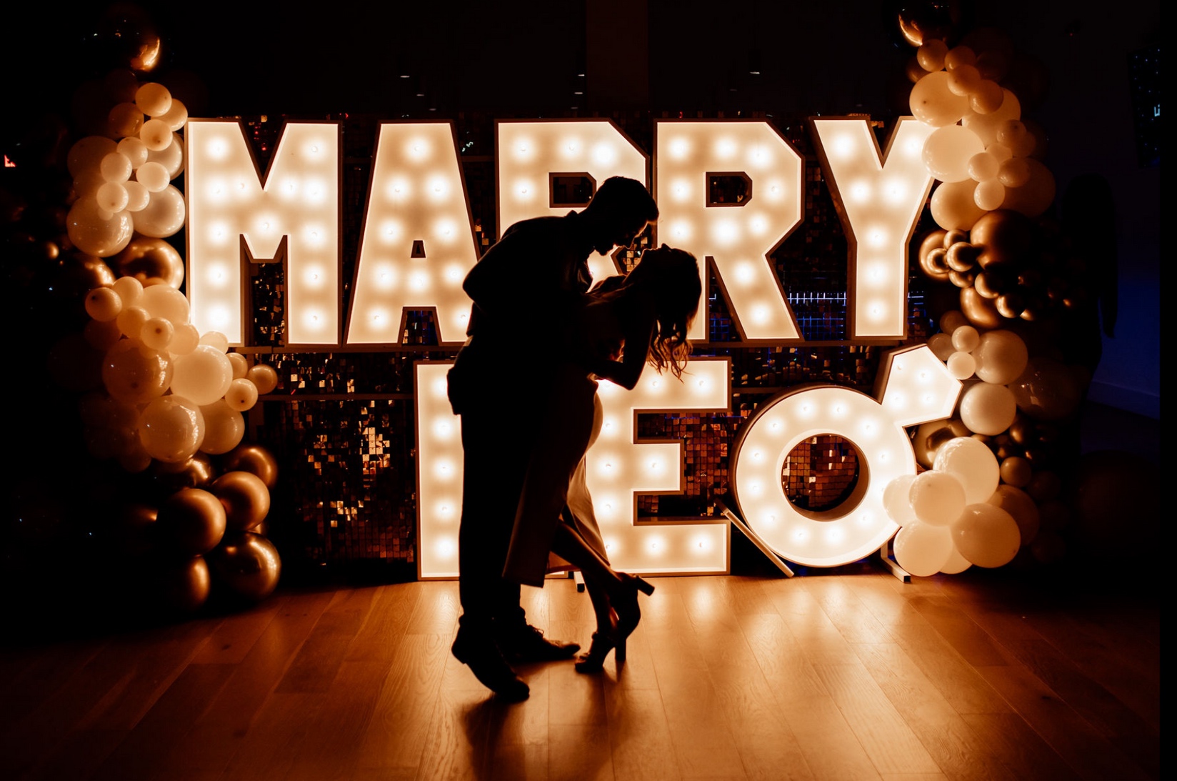 A couple kissing in front of illuminated Marry Me letters